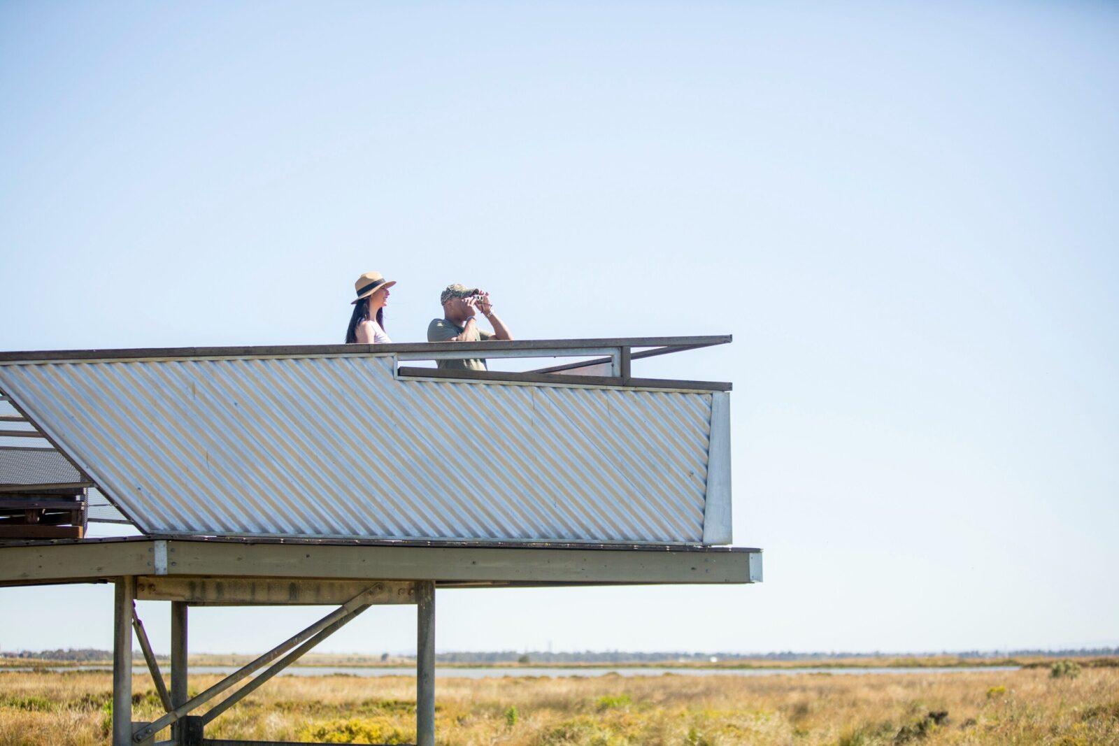 two adults on tower with binoculars looking out to wetlands