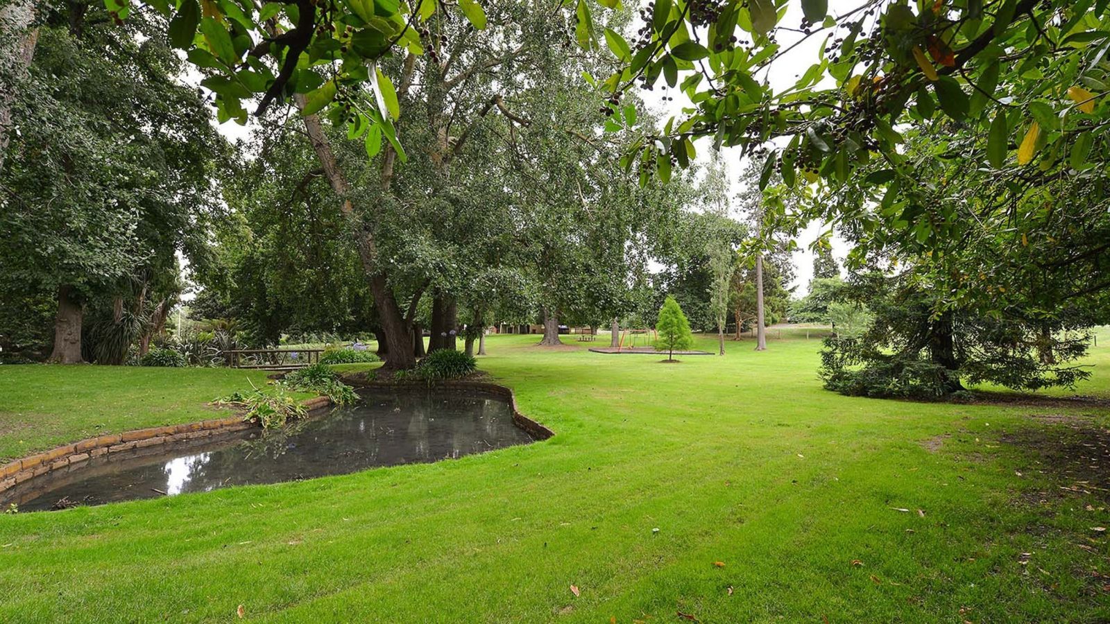 Green garden grounds with small pond to left and playground in far distance