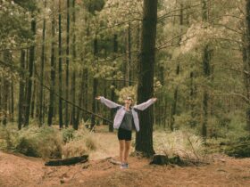 A woman stands with her arms in the air surrounded by trees