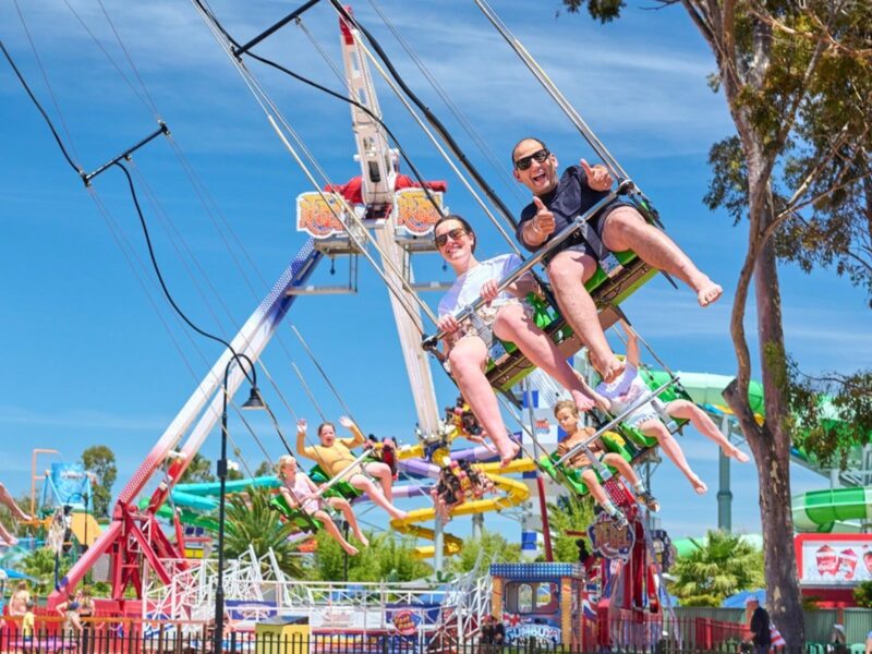 Man with his thumbs up and woman sit on Tree Swing ride at Gumbuya World as they're swung around.