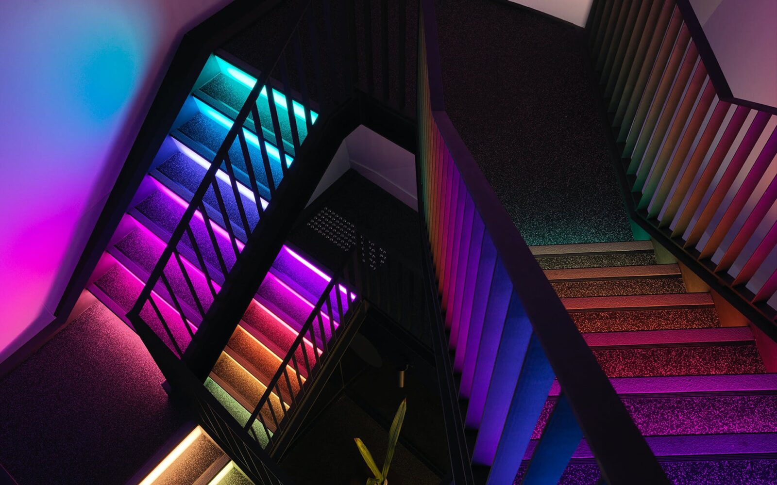 Birds eye view of three flights of stairs inside JAHM. The stairs are lit up in rainbow colours.