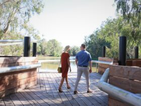 Couple walking on redgum wharf at Koondrook with Murray River in the background