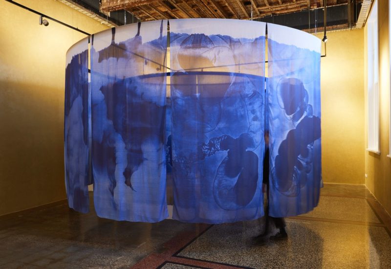 Fabric with blue cyanotype photos hanging in a circle inside a gold room