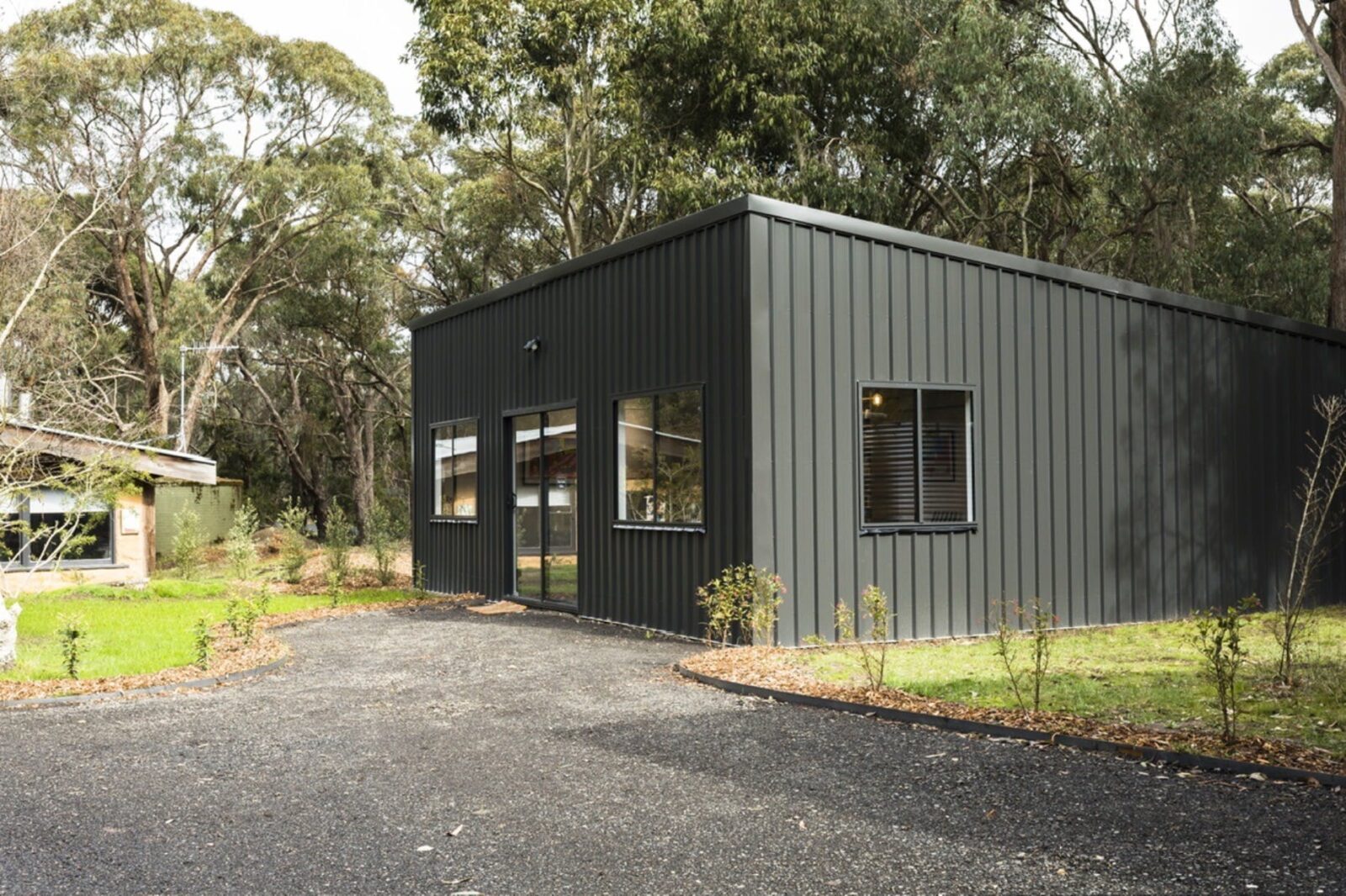 View it outside of gallery, black shed with windows in bush landscape