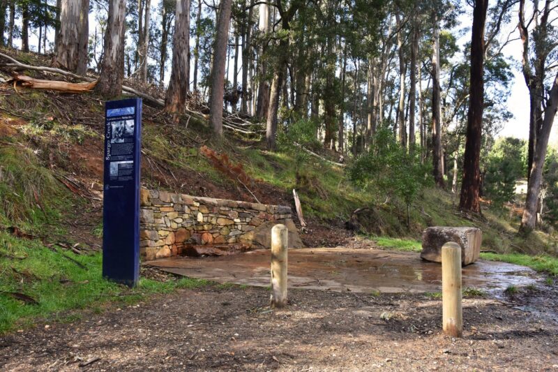 The landscape of Spargo Creek Mineral Spring. A blue sign, a retaining wall, trees