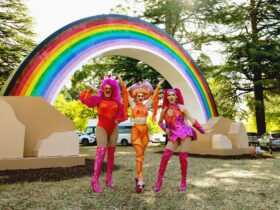 Three drag queens in front of a big rainbow