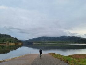 Cyclist on ramp, lake, hills with grass and trees, shadows in water, grey clouds, low cloud on hills