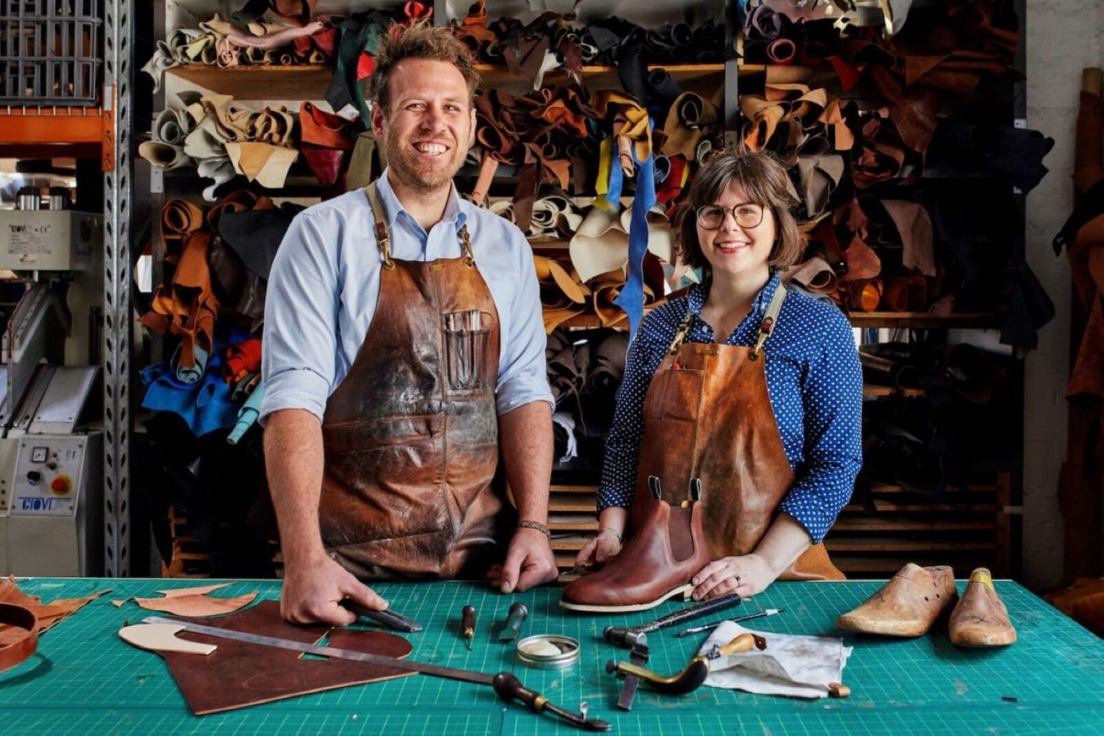 Jess and Krystina standing in front of leather storage with tools laid out on table in front