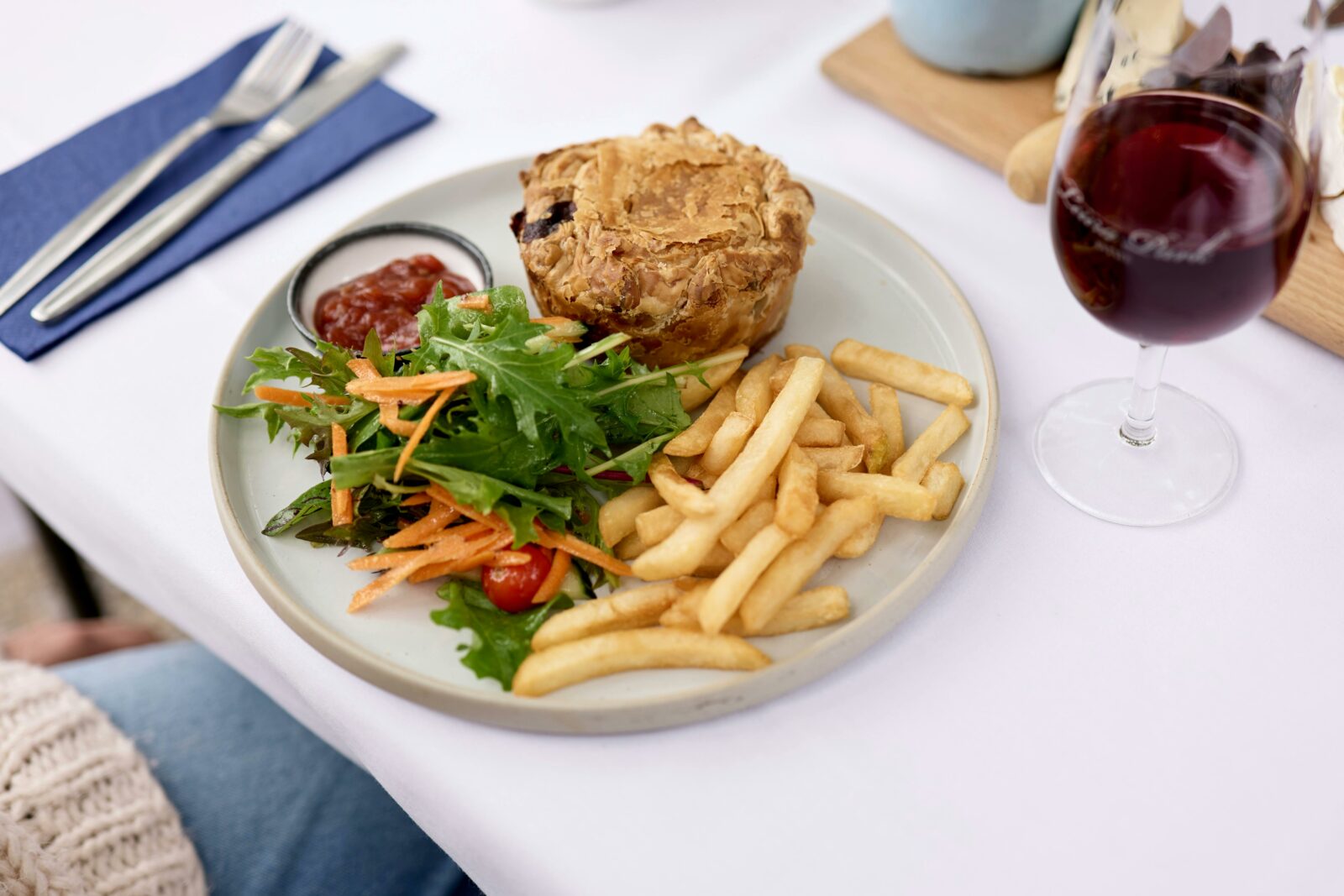 White tablecloth, a plate with a pie, chips and salad, and a glass of red wine
