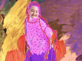Portrait of a girl wearing a purple shirt smiling, against a colourful painting backdrop