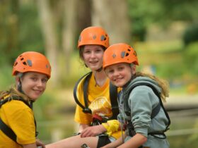 3 young girls wearing orange helmets preparing to abseil