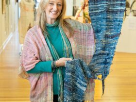 Prue Simmons holds a blue SAORI woven wall hanging in an exhibition gallery