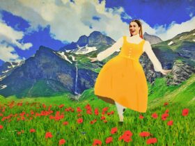 woman in yellow dress standing in front of alps surrounded by red flowers
