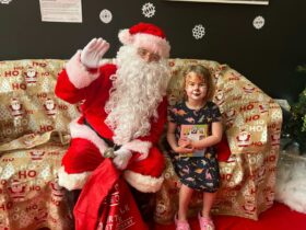 Santa sits on a couch next to a young girl for a special Santa photo