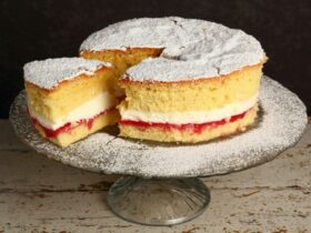Delicious sponge cake layered with jam and cream sitting on cake stand, dusted with icing sugar.