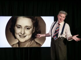 A man talking in front of a screen with a woman's face on it