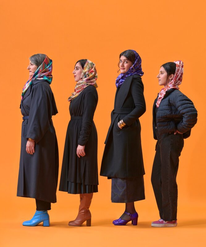 Four women standing in a row donning colourful scarves on an orange background.