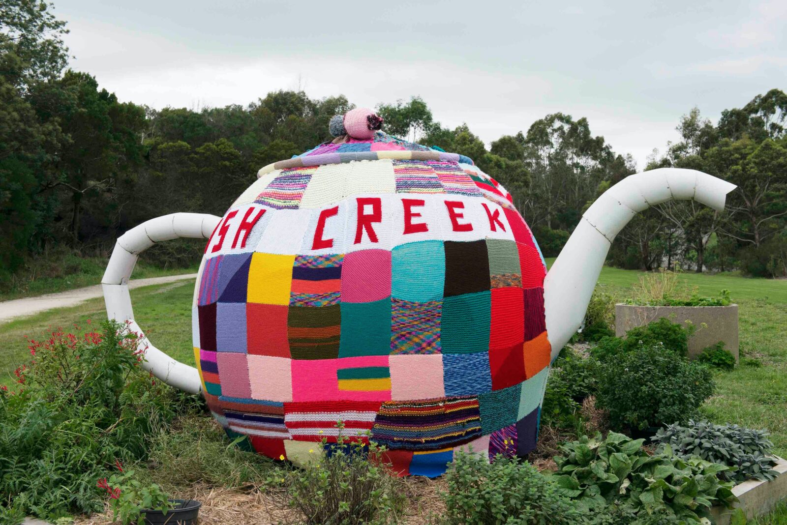 Knitted tea cosy on a big teapot in the Fish Creek Commmunity Garden