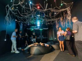 visitors stand and lay on bean bags to look up at an artwork featuring a network of wires and lights