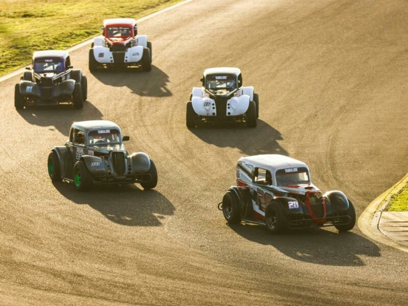 Five legend cars racing around a corner on a racetrack