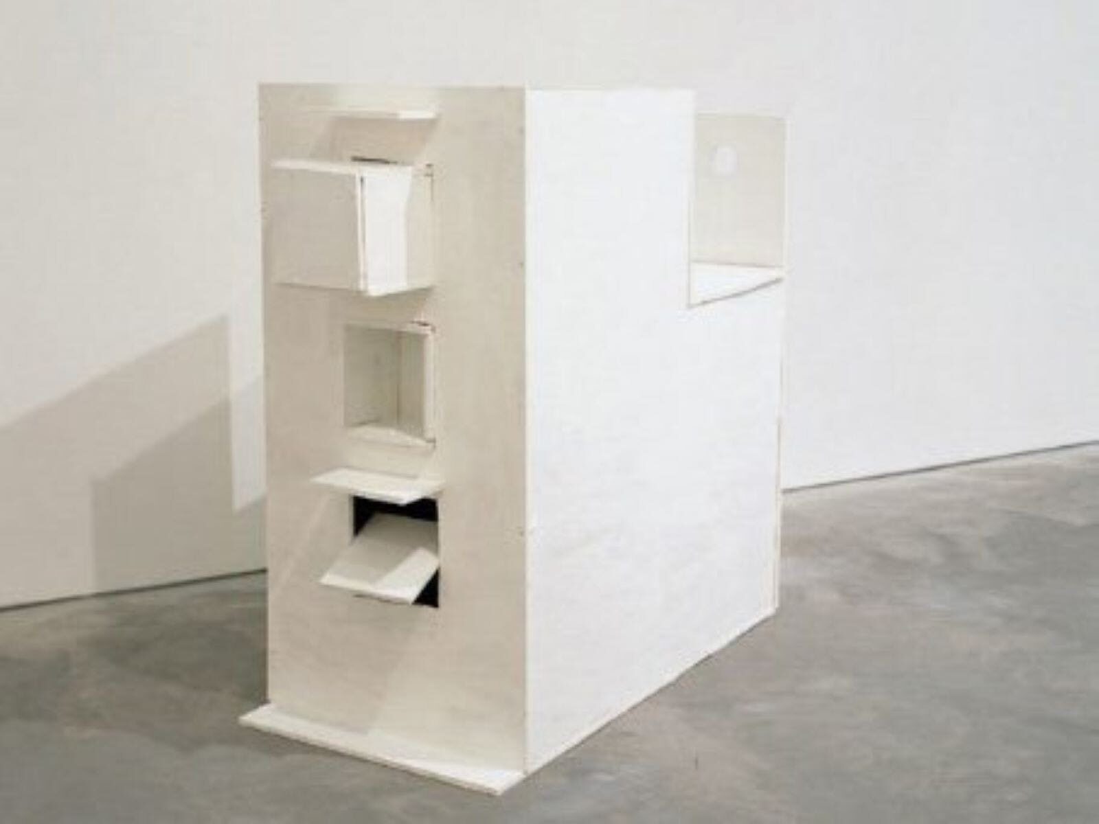 A white wooden sculptor of a building on concrete floor, against a white wall