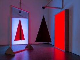 Installation with luminous red panel, mirror and suspended triangular shapes.