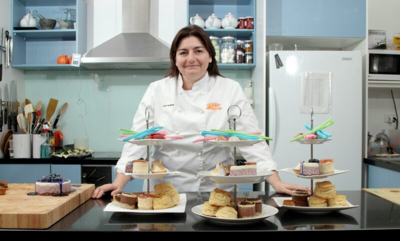 Chef standing behind the bench with three multilevel cake stands with cakes and lollies