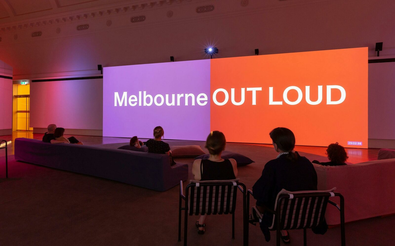People sitting on couches in front of two screens that say Melbourne Out Loud