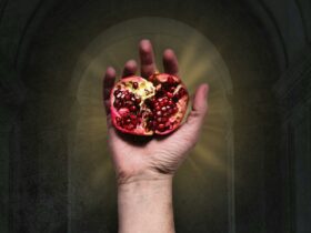 A hand holds a pomegranate, symbol of Persephone against a dark, glowing portal background