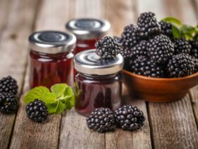 Three jars of blackberry jam surrounded by a bowl of fresh blackberries.