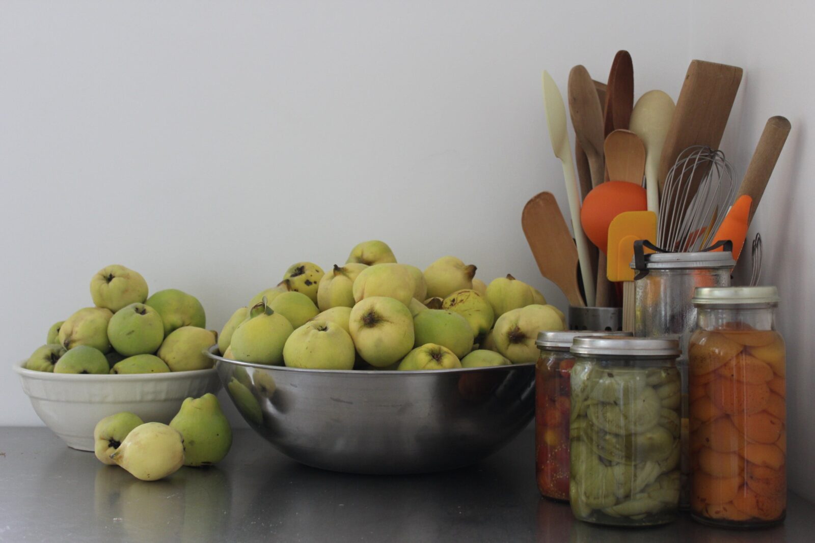 Bowls of quinces sitting on a bench with vacola jars of preserves and kitchen tools