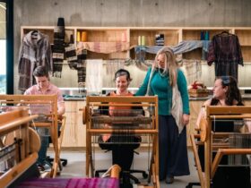 Three women seated at looms with instructor looking over