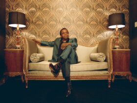 Lee Fields sitting on a couch with his legs crossed, looking away from the camera.
