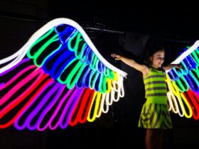 A young girl standing in front of colourful neon wings at night time