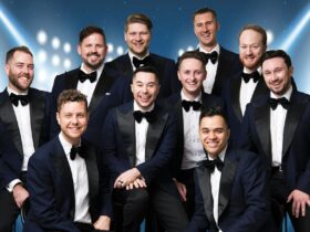 The Ten Tenors posed in suits in front of a blue background with scattered bright lights