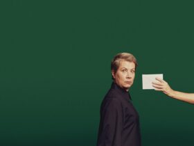 Actor against a green backdrop looking surprised with a hand held out holding an envelope
