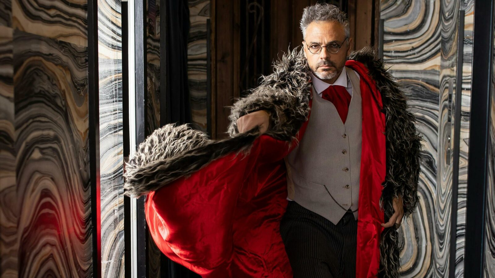 A well dressed man swooshes a fur coat with bright red inner lining.