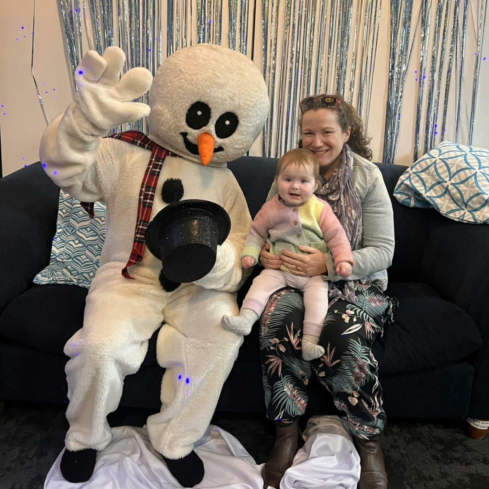 Frosty the Snowman poses on a couch with a mother and baby for a photo