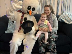 Frosty the Snowman poses on a couch with a mother and baby for a photo