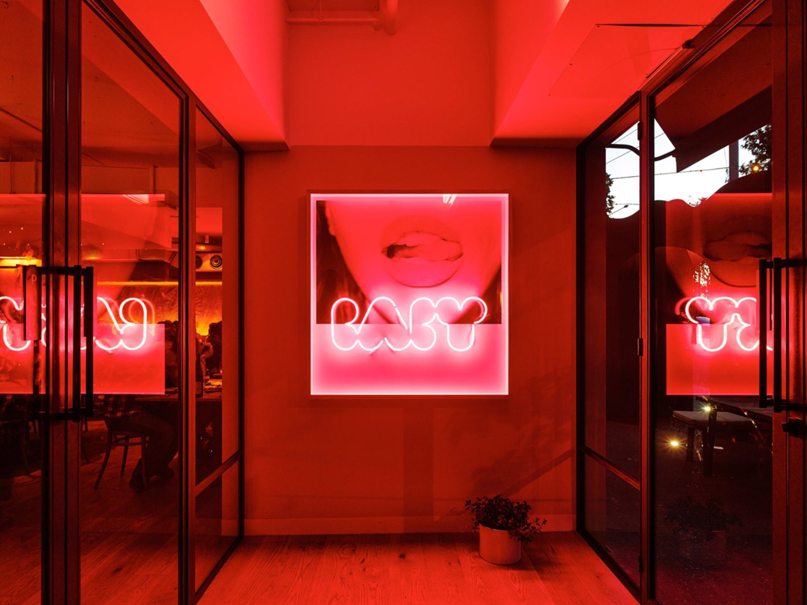 Room with glass doors on either side, facing a light box image of a female red neon sign "Baby".