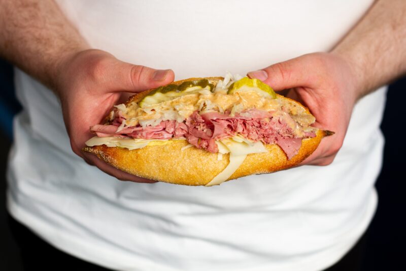 Hands holding a Reuben baguette sandwich