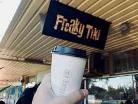 Hand holding Freaky Tiki branded white takeaway coffee cup in front of Freaky Tiki venue sign