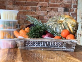 basket of vegetables, including pumpkin, tomatoes, red onion and carrots next to containers of food