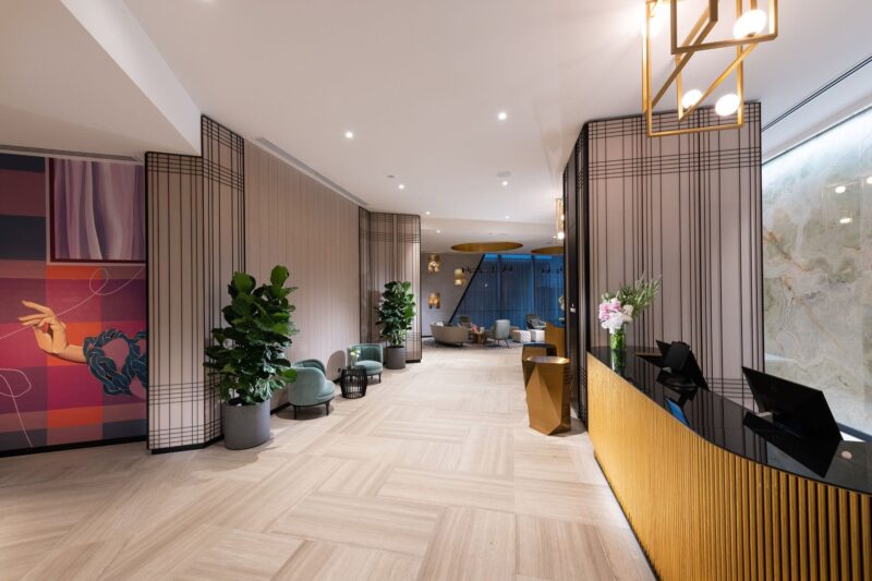 An image of a hotel lobby with artwork, gold reception desks and plants, visibility to the lounge