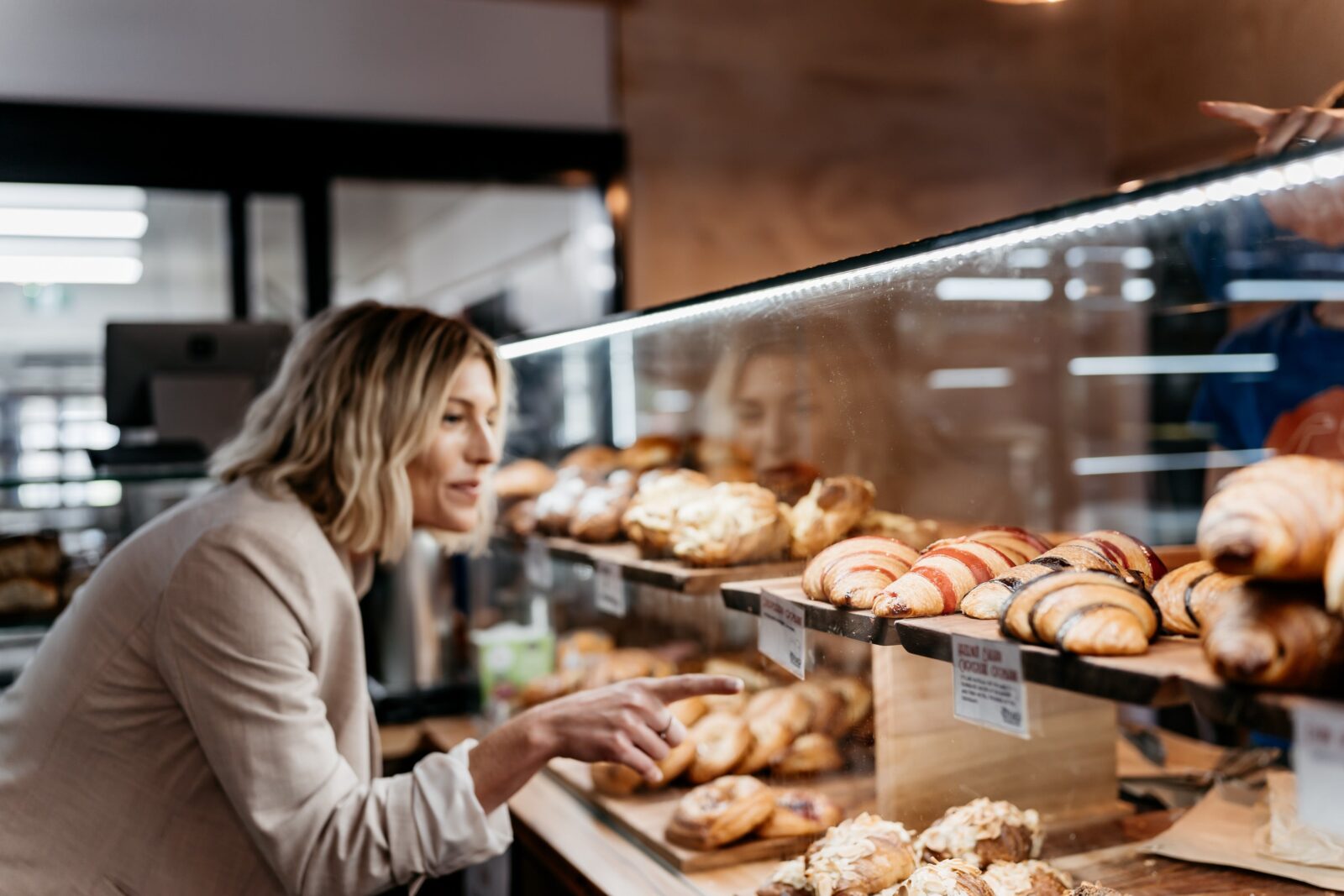 A woman selects a croissant from a display cabinet of pastries
