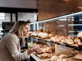 A woman selects a croissant from a display cabinet of pastries