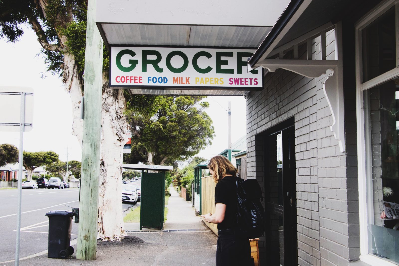 A customer waiting outside the corner store underneath a large sign that says 'GROCER'