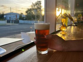 person holding a glass of beer, window seating, with sunset in the background.