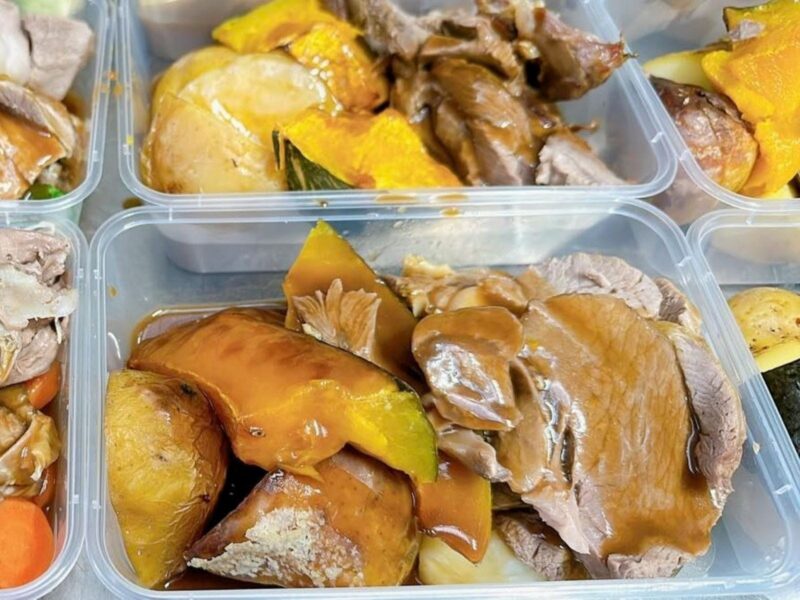Close up of roast lam pieces with vegetables and gravy in a takeaway container