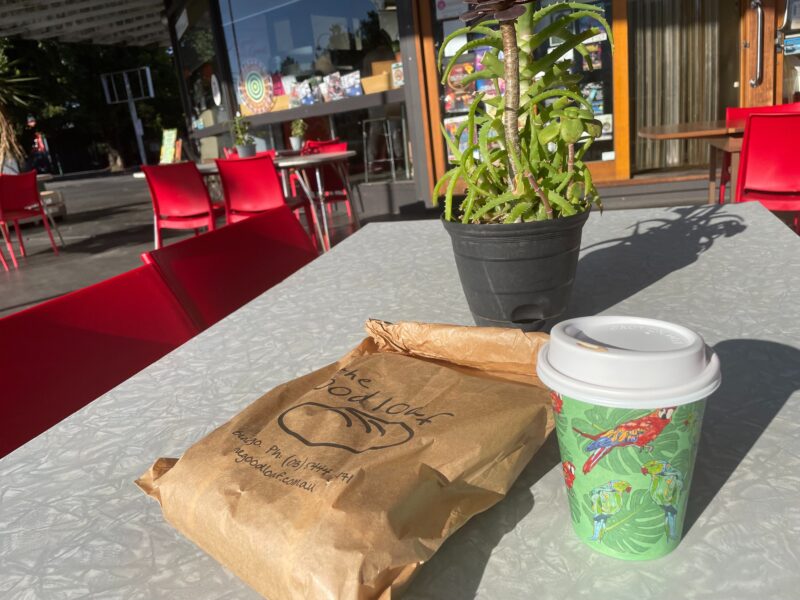 Takeaway paper bag and takeaway coffee sitting on a sunny table outdoors